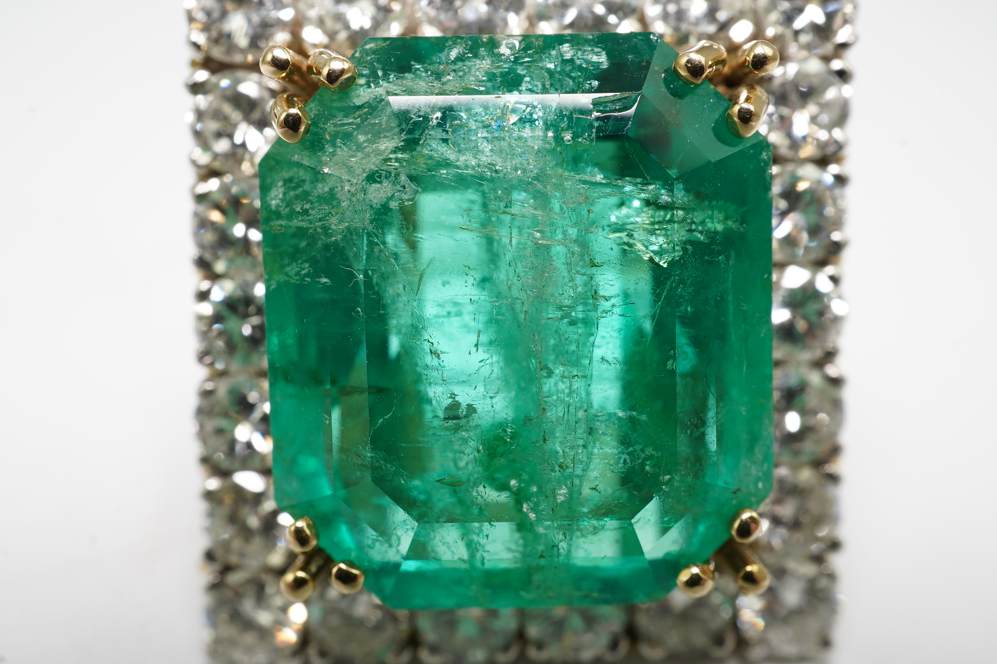 A Stern 18ct white and yellow gold, emerald and diamond dress ring, the central green emerald cut emerald approximately 8.0ct and surrounded by twenty two circular cut diamonds, approximately 2.7ct total